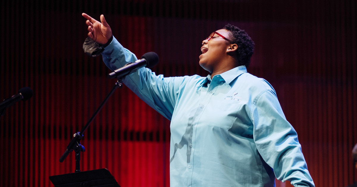 VocalEssence Singers Of This Age member sings into a microphone with hand outstretched, Photo Credit: Adja Gildersleve