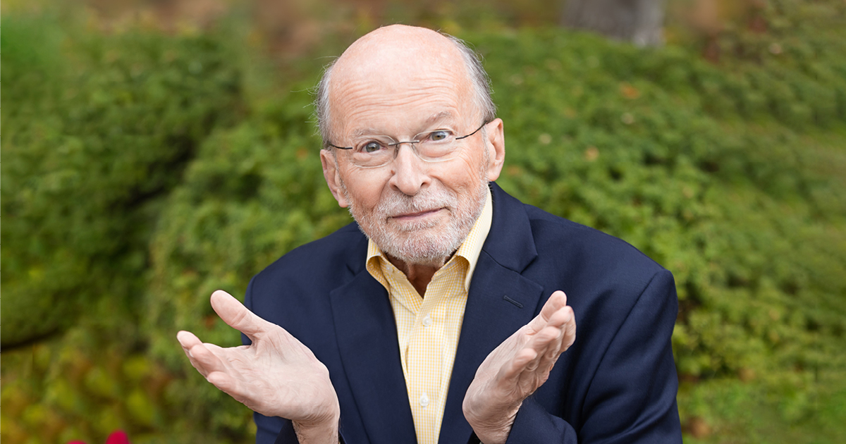 Philip Brunelle, conductor, looks into the camera smiling with his hands open and near his face. Photo Credit: Anna Min