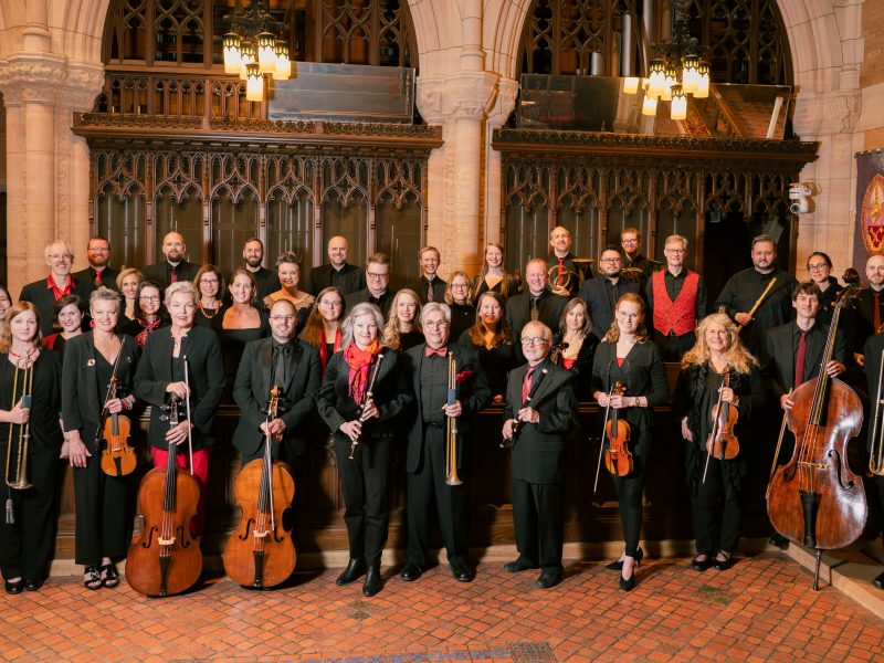 People wearing black and red and holding Baroque instruments pose for a photo.