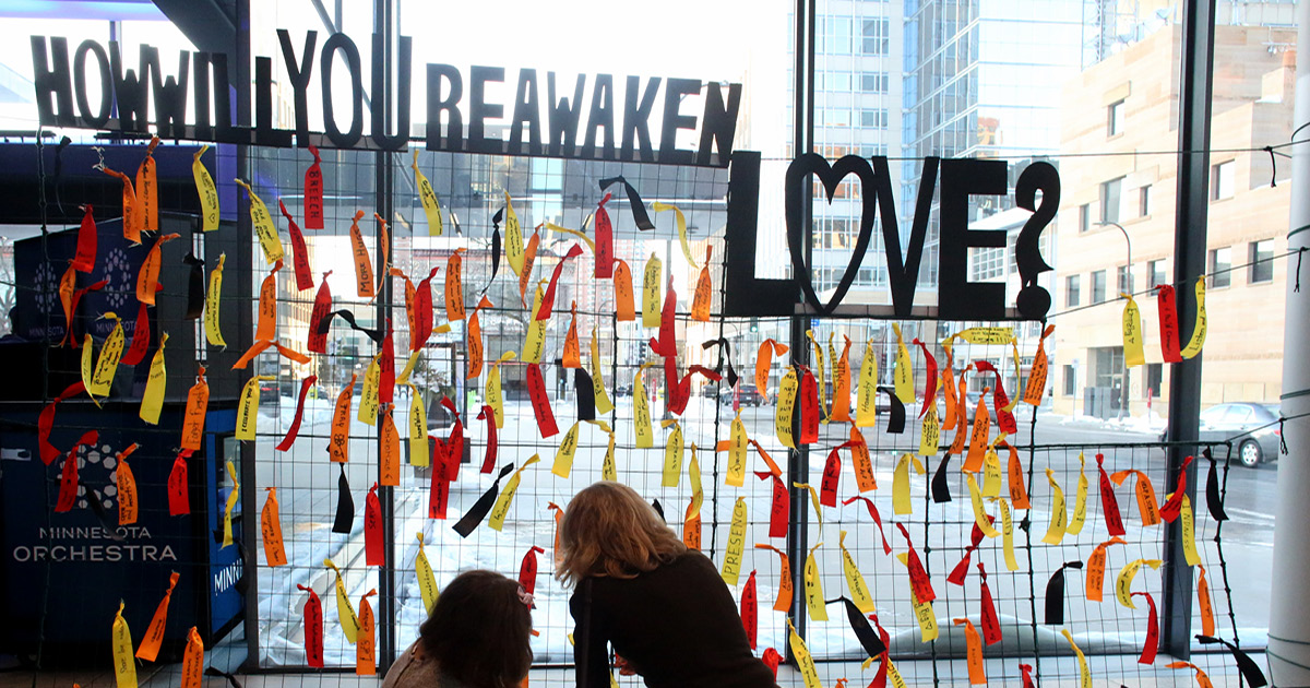 People in front of display with different colored ribbons and the question, How Will You Reawaken Love? Photo credit: Kyndell Harkness