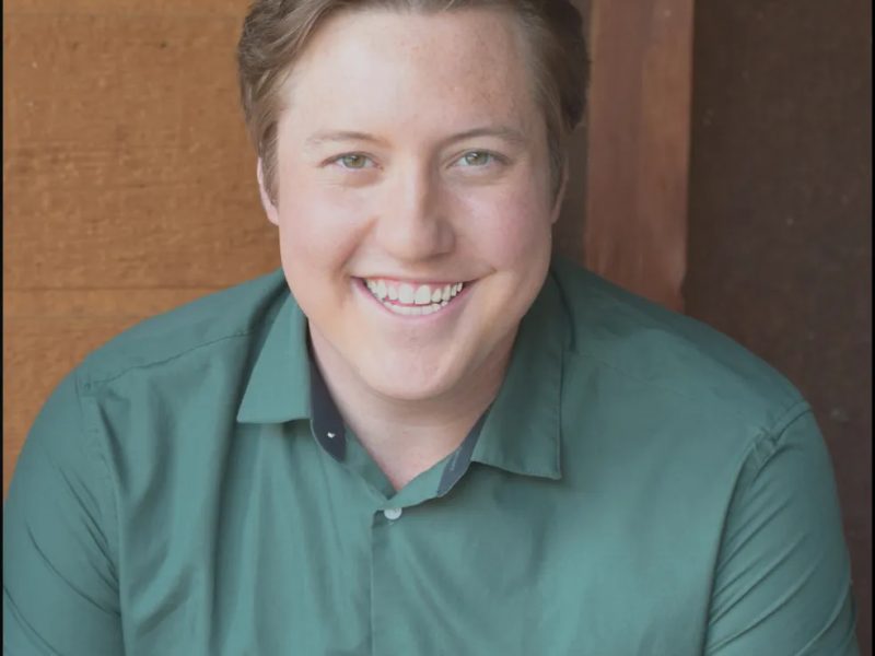 Person with short brown hair wearing a green button down top looking at the camera and smiling.
