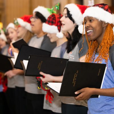 People wearing red and white Santa hats holding black folders and singing.