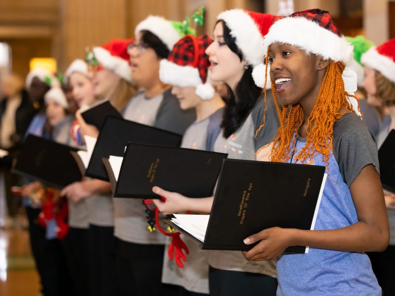 People wearing red and white Santa hats holding black folders and singing.