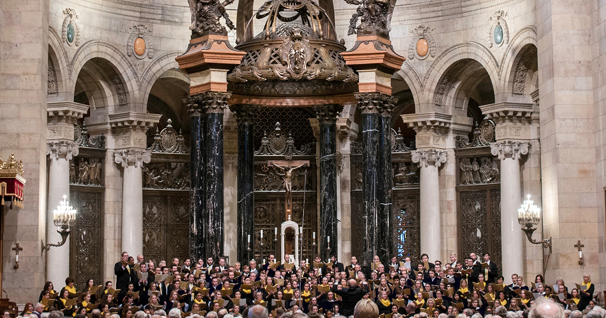 Many singers perform in front of an audience in the ornate sanctuary of the Cathedral of Saint Paul that features a baldachin with black and gold marble columns that has a bronze latticework canopy. Photo Credit: Bruce Silcox