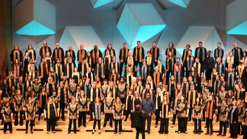 VocalEssence singers wearing black and multicolored stoles perform on stage for the annual WITNESS concert. Photo Credit: Kyndell Harkness