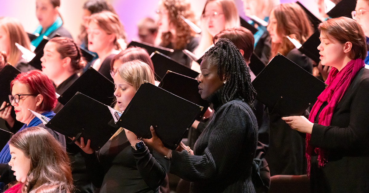 VocalEssence singers holding black folders and wearing black with colorful scarves perform at Northrop. Photo Credit: Anna Min