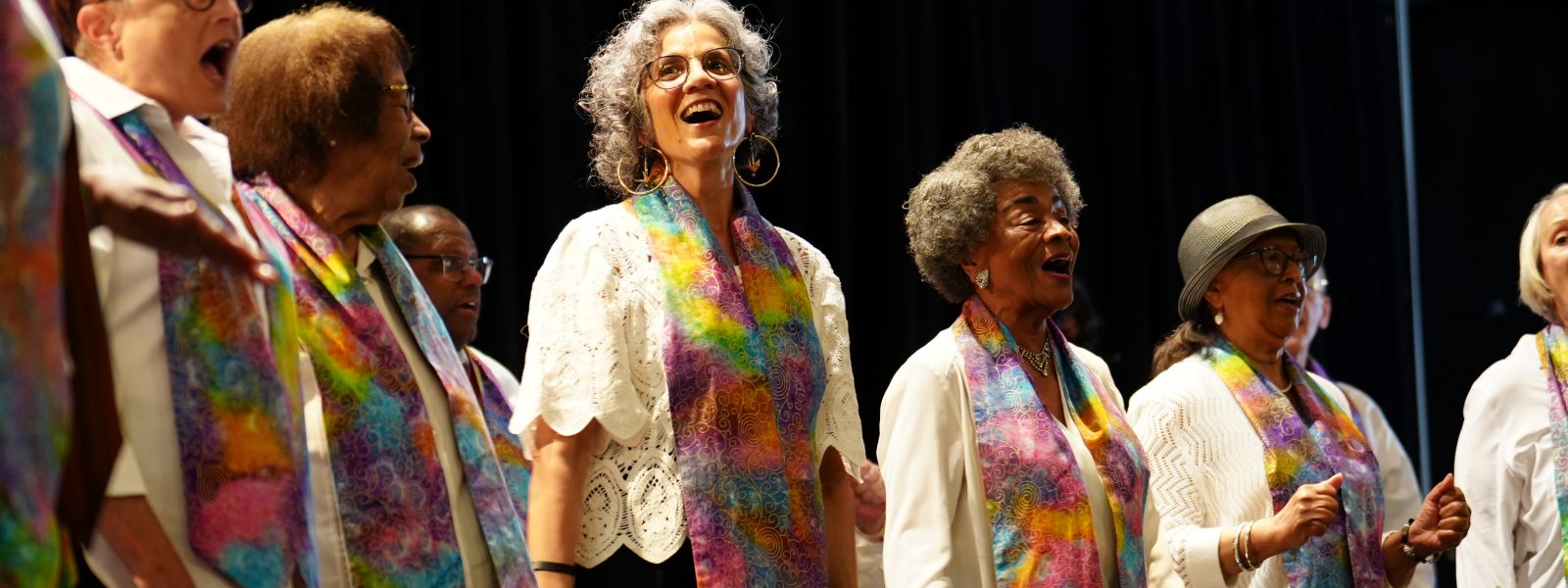 Adult Vintage Voices members wearing white shirts with colorful stoles and singing. Photo Credit: Novelli Jurado