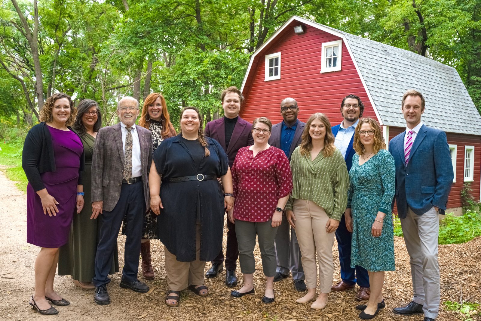 Members of the VocalEssence staff pose for a photo in front of a red barn surrounded by greenery. Photo credit: Novelli Jurado, Novart Media