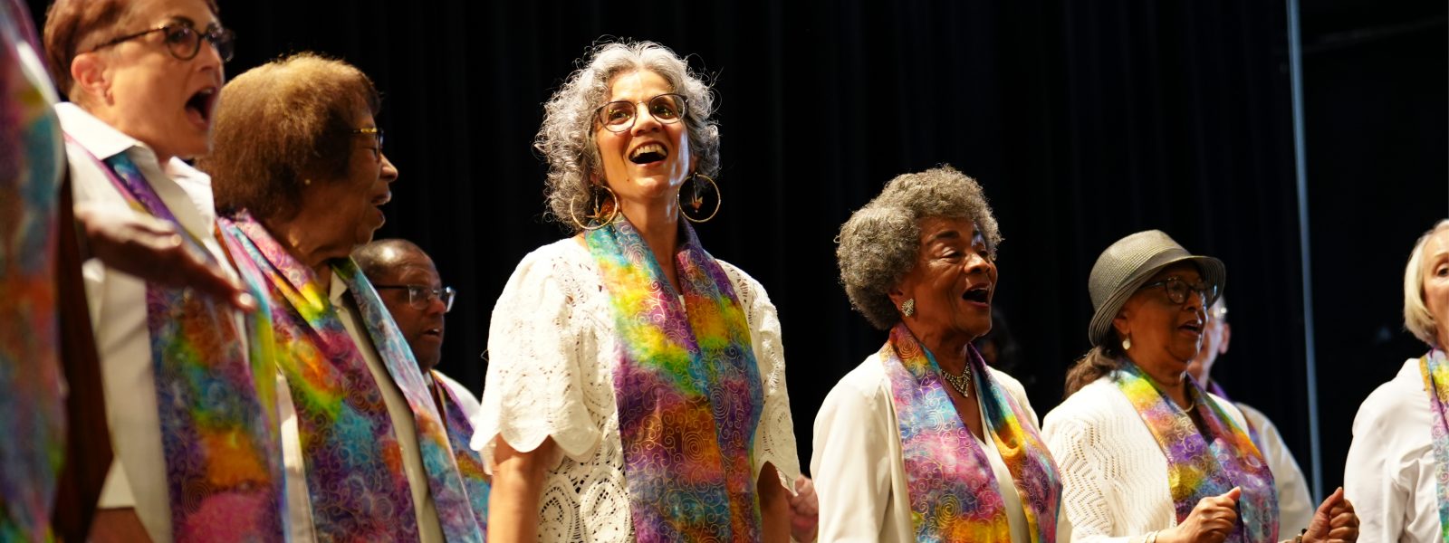 Vintage Voices Singers performing wearing white shirts and multi-colored pastel stoles. Photo credit: Novart Media.
