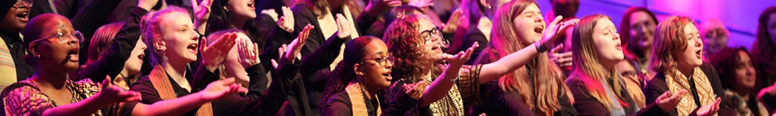 VocalEssence singers wearing black with multicolored stoles perform while holding their arms forward on stage for the annual WITNESS concert. Photo Credit: Kyndell Harkness