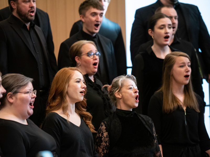 VocalEssence Ensemble Singers wearing black perform with joyful expressions. Photo Credit: Bruce Silcox