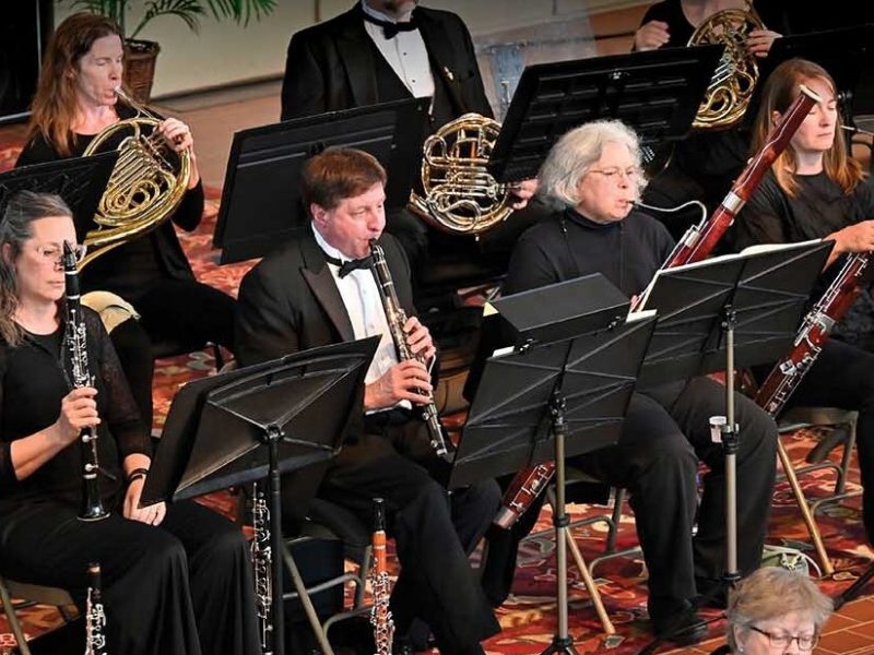 Members of the Metropolitan Symphony Orchestra wearing black, sitting, playing their instruments, with black music stands.