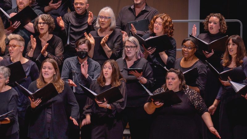 Members of the VocalEssence Chorus wearing black, holding black folders, and singing. Photo Credit: Novart Media