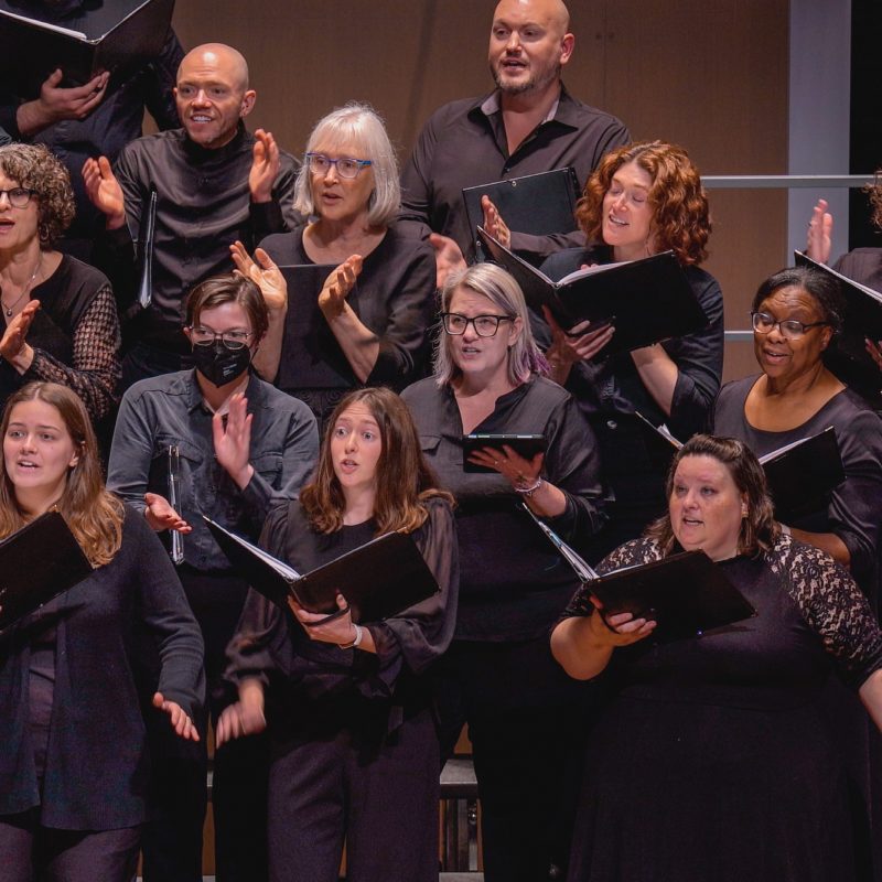 Members of the VocalEssence Chorus wearing black, holding black folders, and singing. Photo Credit: Novart Media