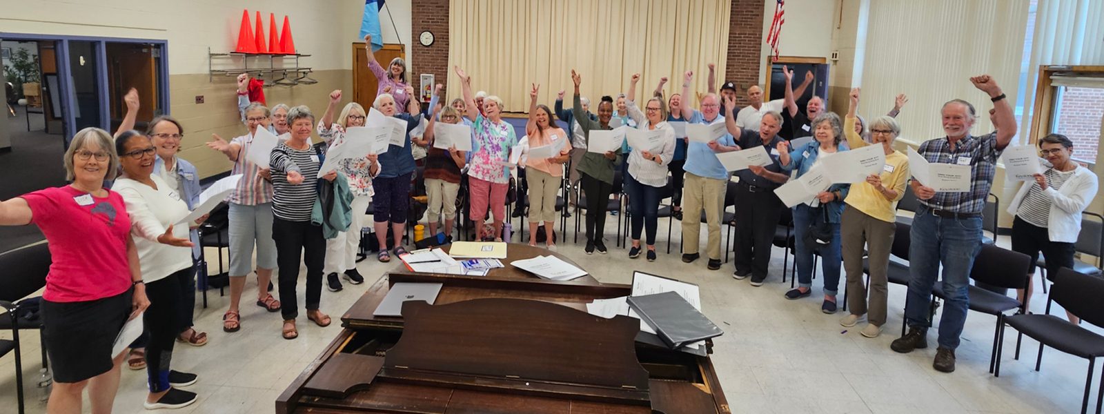 Image of singers with their hands up around a piano. Photo Credit: Robert Graham